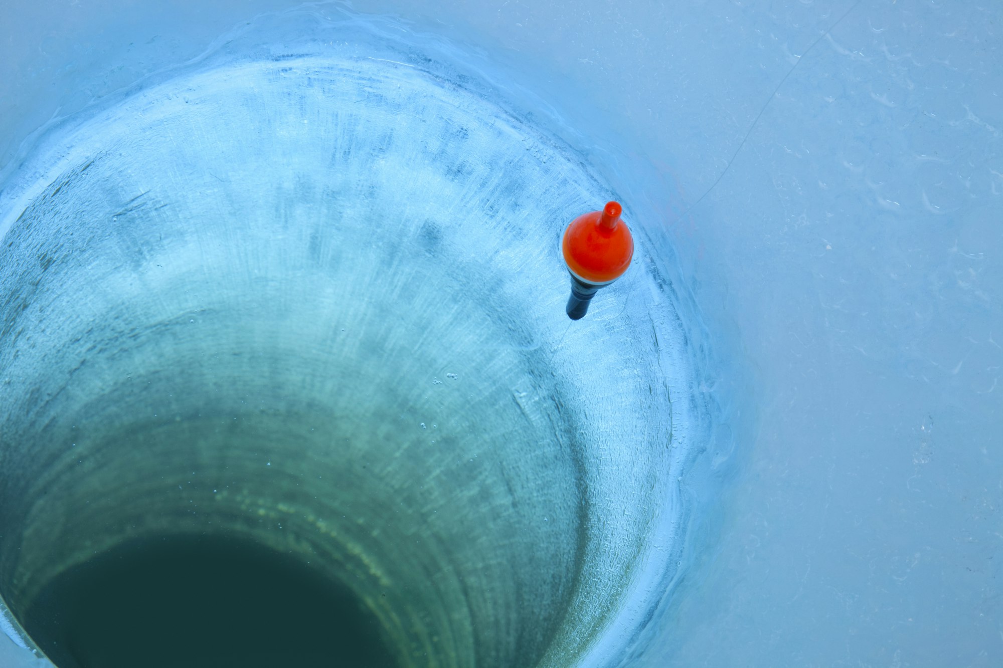 Red bobber and fishing line in an ice fishing hole in a Minnesota lake